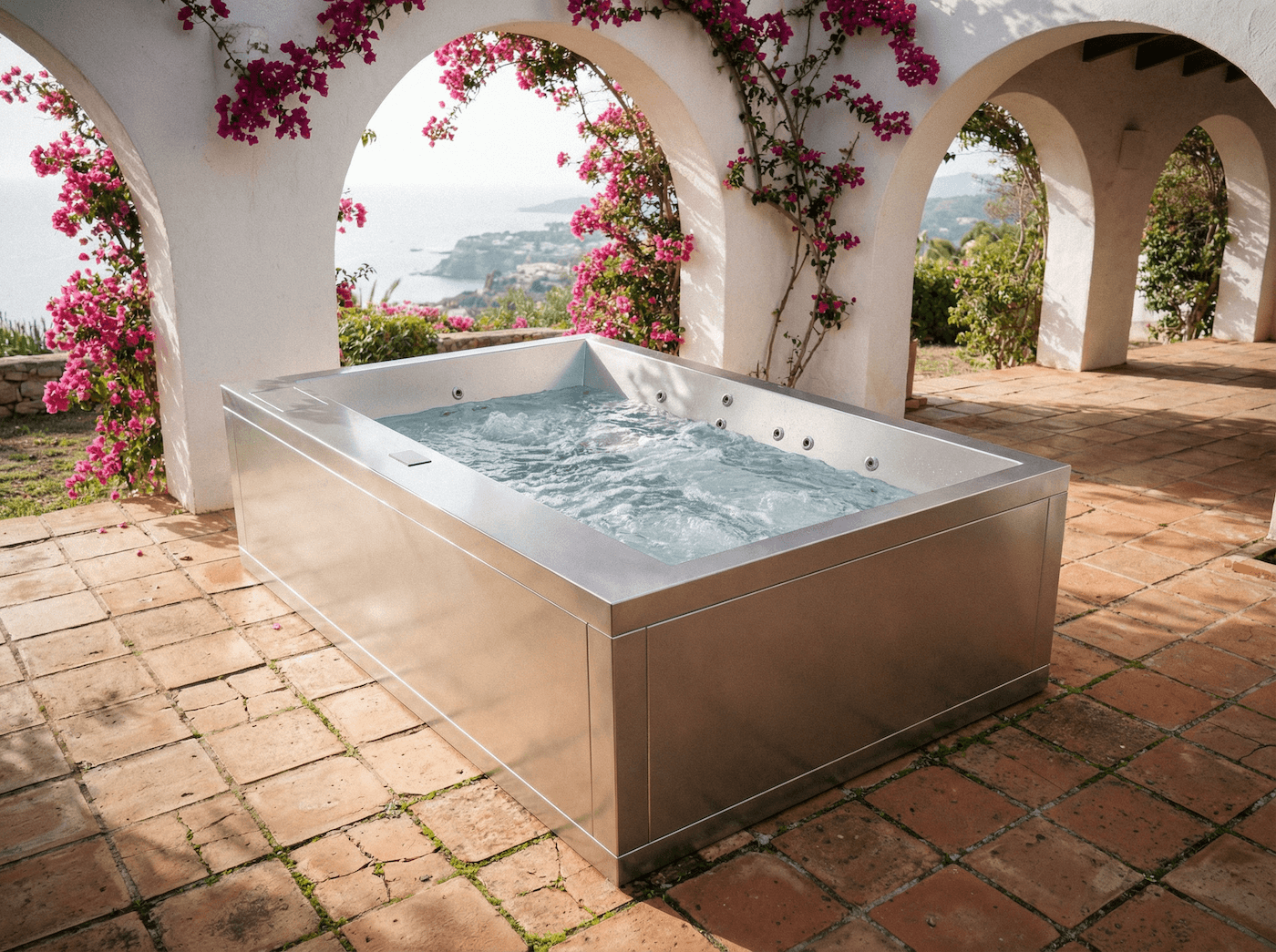 Outdoor hot tub under arches with sea view and pink flowers.