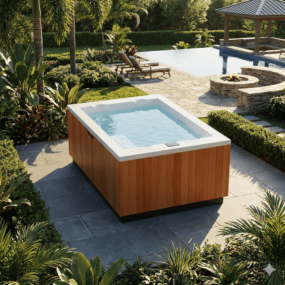 A wood-paneled swim spa sits on a stone patio in a lush backyard next to a pool.
