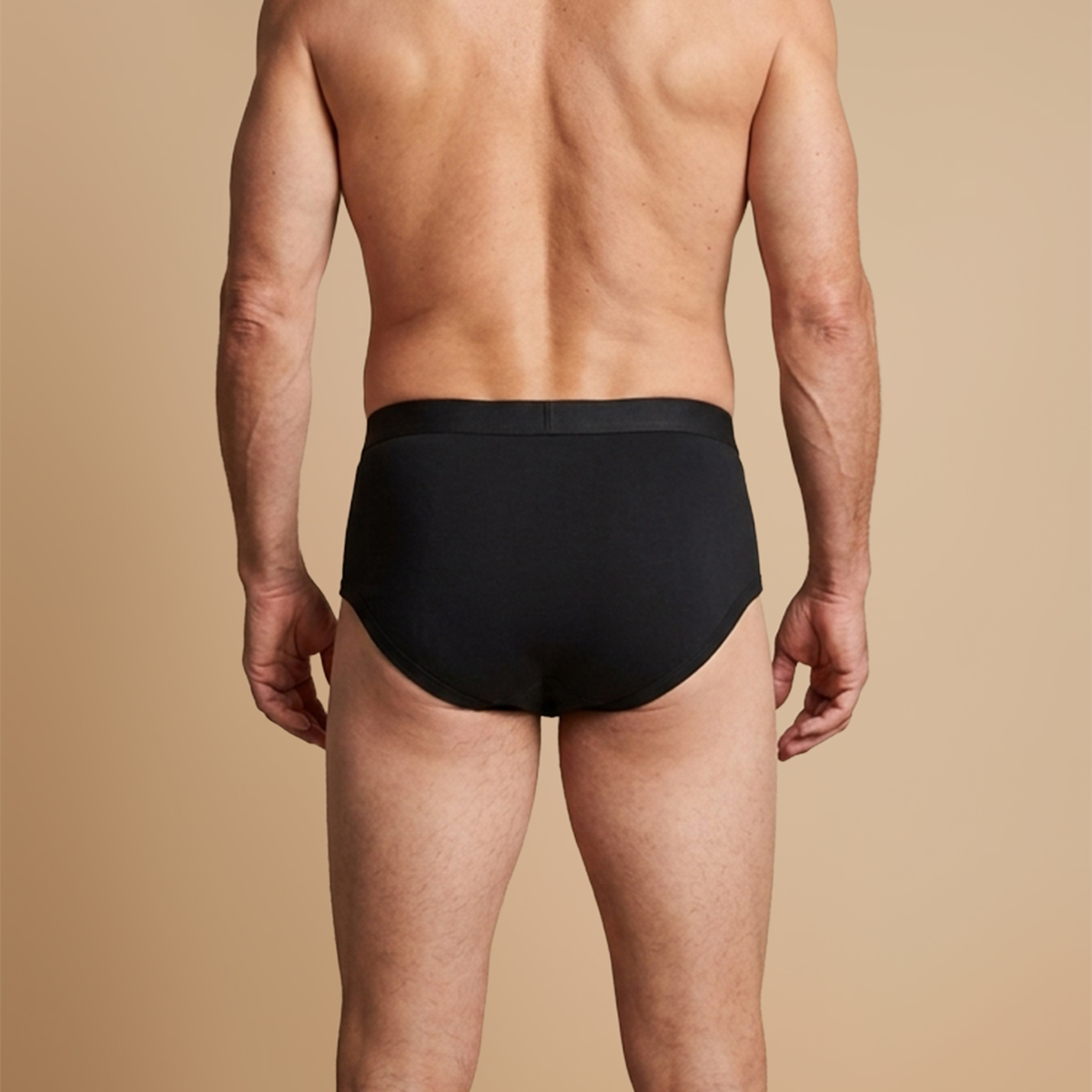 Rear view of a man wearing black briefs against a solid tan background.
