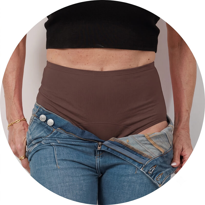 A person wearing brown high-waisted underwear and a black top, with their blue jeans unzipped and open.