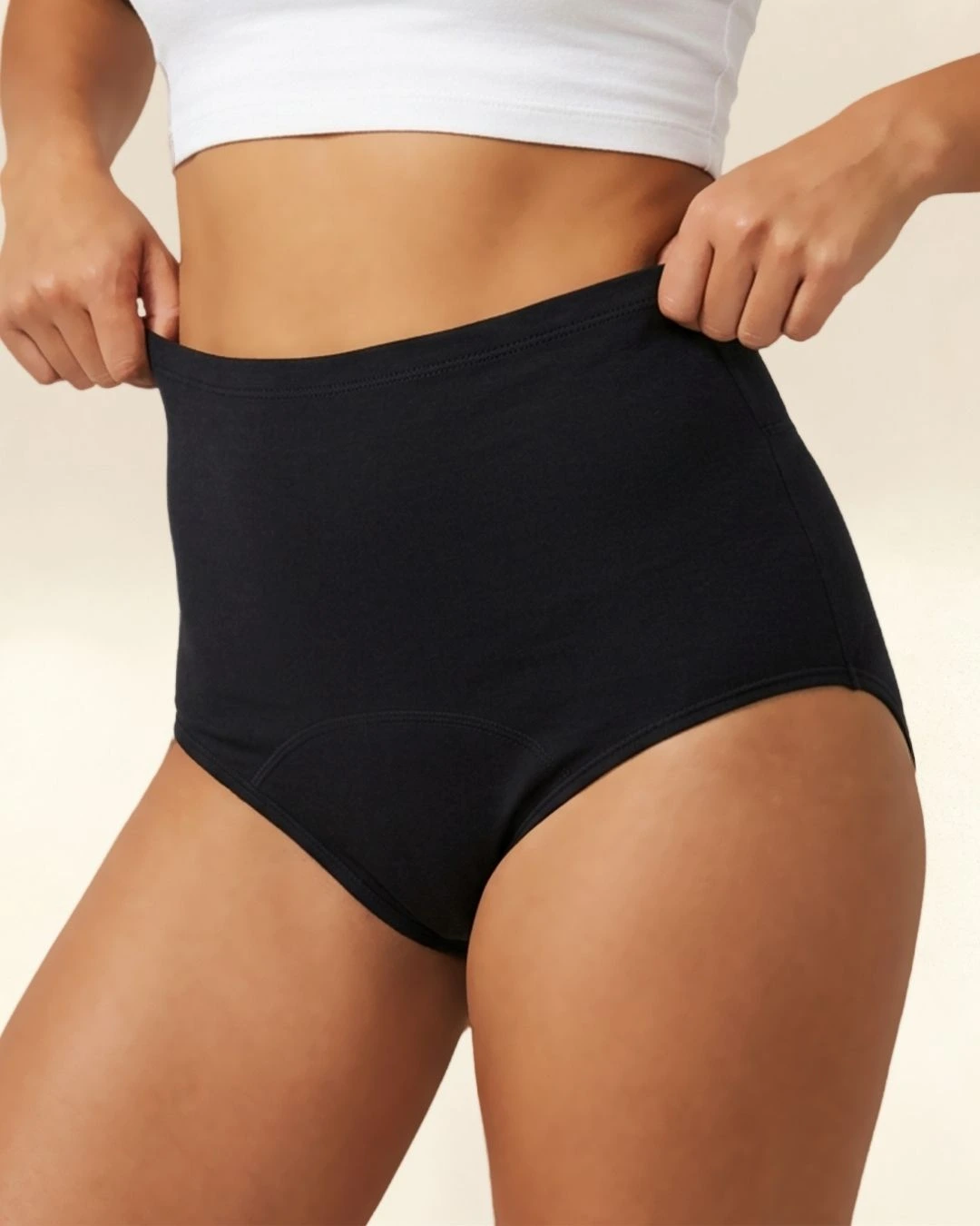 A person wearing a white crop top pulls on the waistband of black high-waisted underwear.