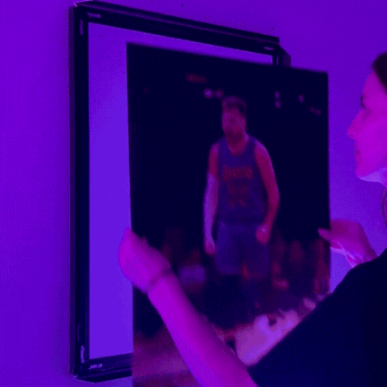 Person placing a basketball poster on a wall under purple lighting.