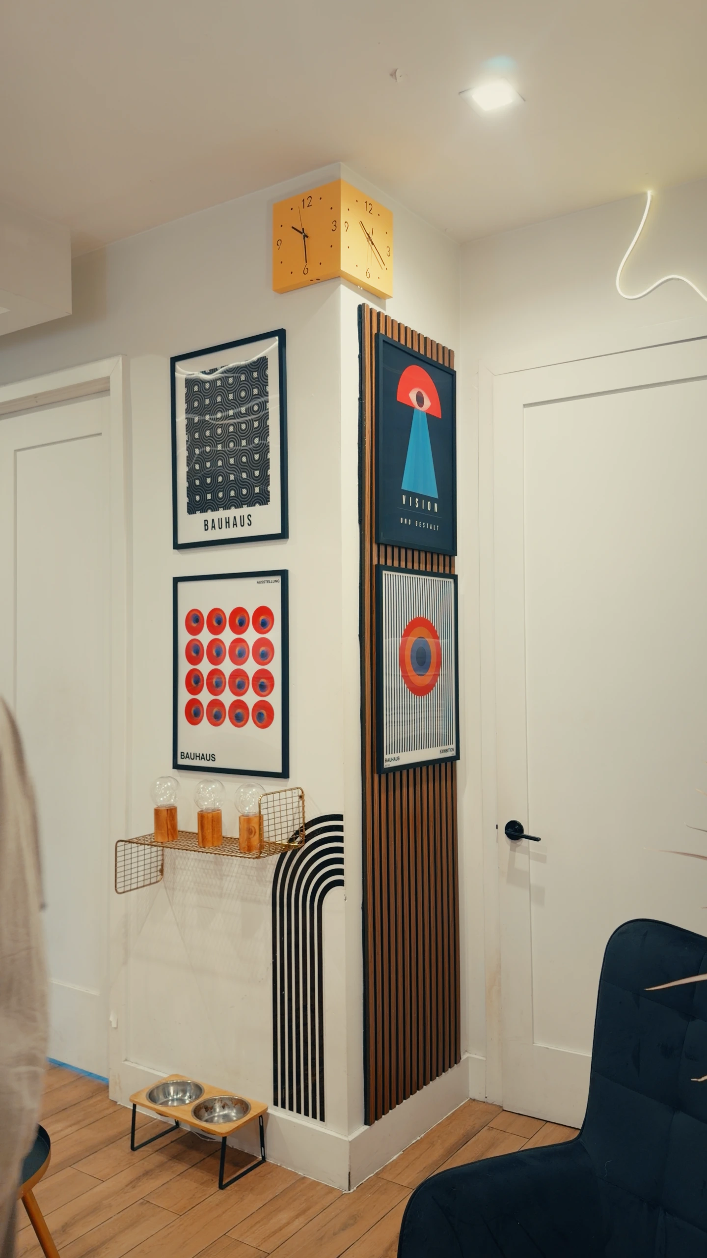 A decorated corner of a room with modern art posters, a yellow corner clock, and pet bowls.