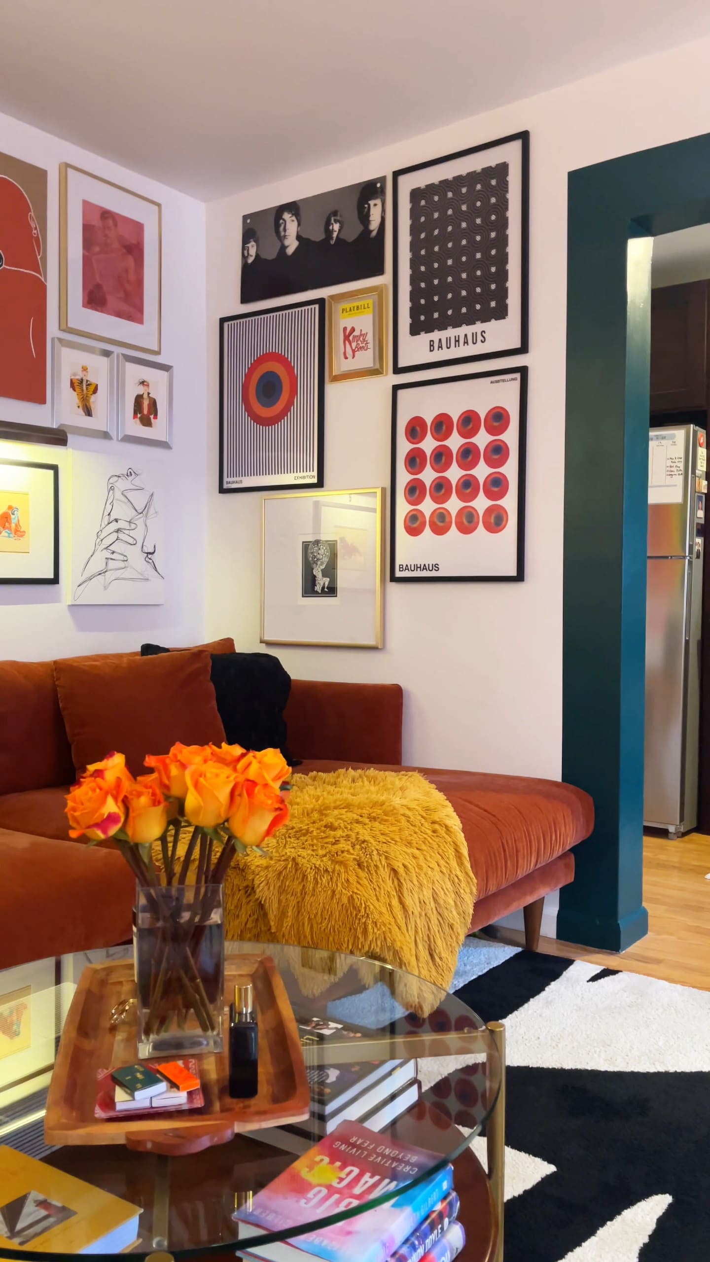 A living room with an orange sectional sofa, a gallery wall, and a vase of orange roses.
