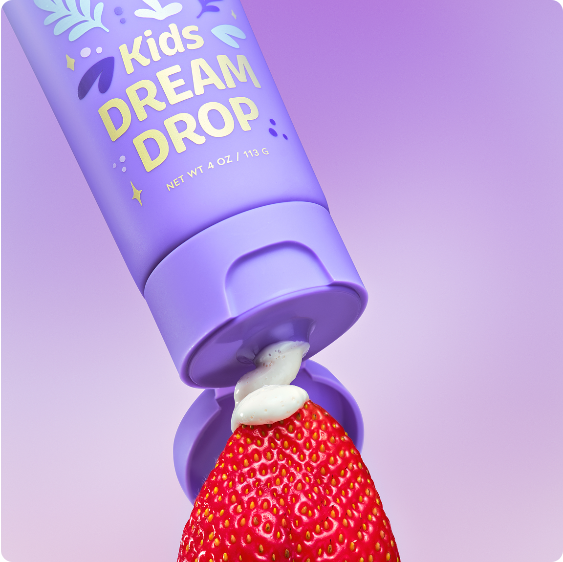 A purple tube of 'Kids DREAM DROP' squeezing white cream onto a fresh strawberry against a lavender background.