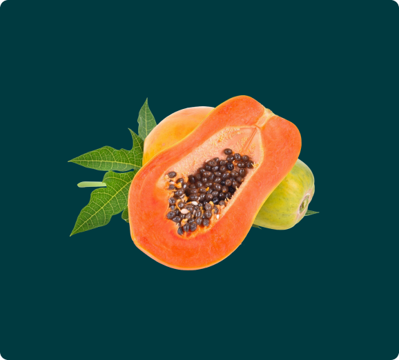 A ripe papaya sliced in half revealing its seeds, resting with whole papayas and leaves.