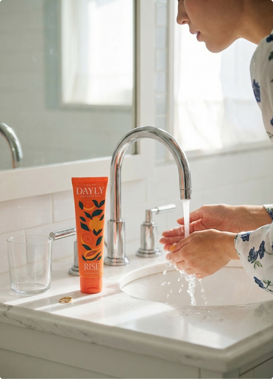 A person washes their hands in a bathroom sink next to an orange tube of Dayly Rise cleanser.