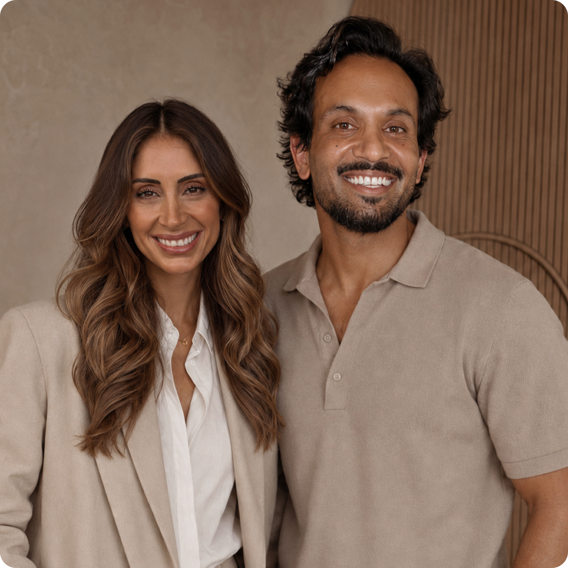 A man and a woman in neutral-colored clothing stand side-by-side, smiling at the camera.