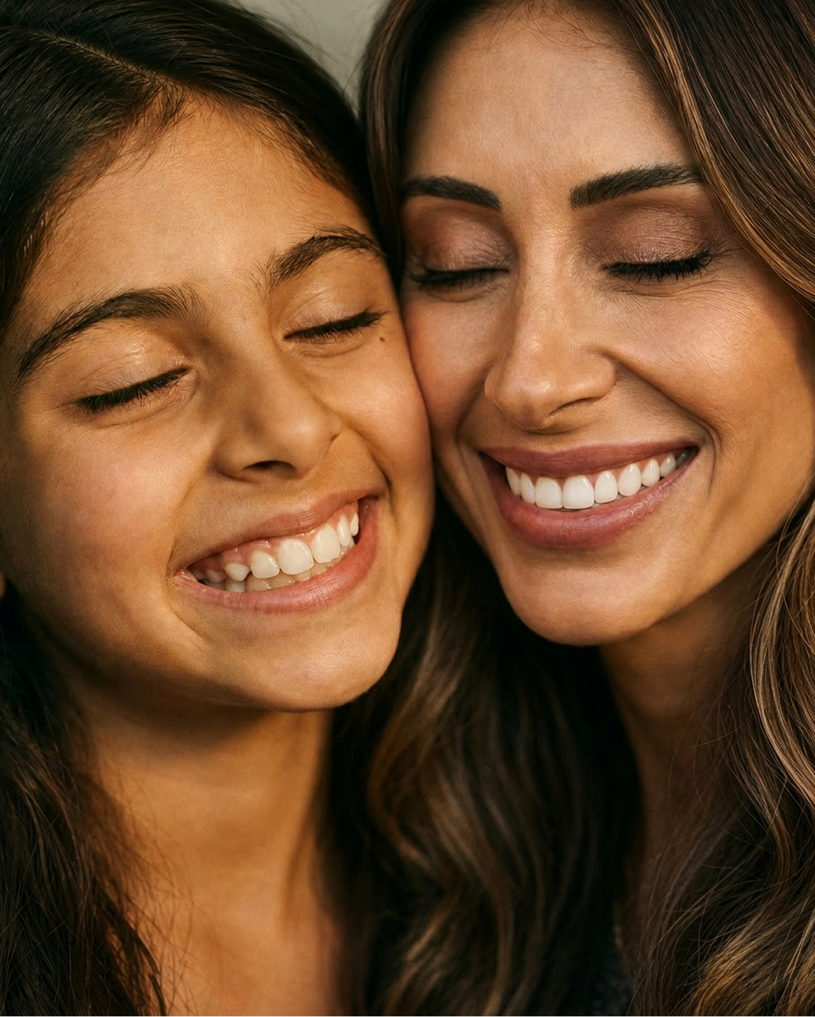 A close-up of a woman and a young girl smiling with their eyes closed, their cheeks pressed together.