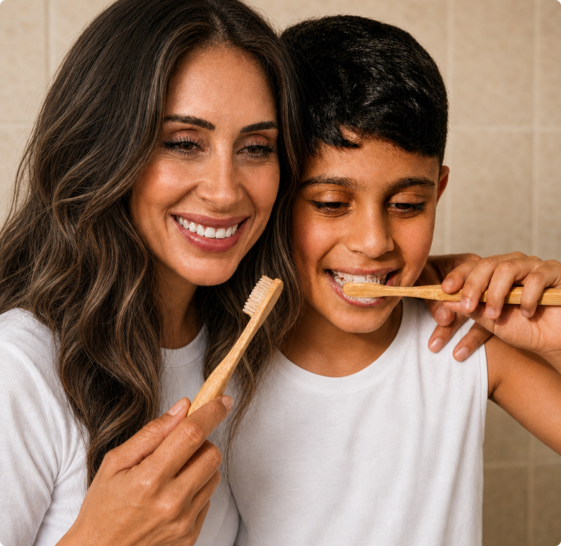 A smiling woman and a young boy brushing their teeth together with bamboo toothbrushes.