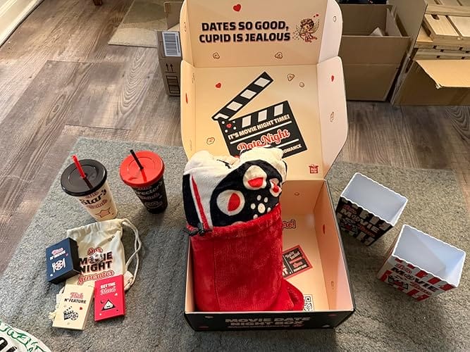 An open movie date night box with its contents, including cups, popcorn boxes, and a blanket, laid out.