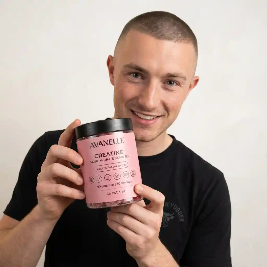 A smiling man with a buzz cut holds a jar of Avanelle Creatine Monohydrate Gummies.