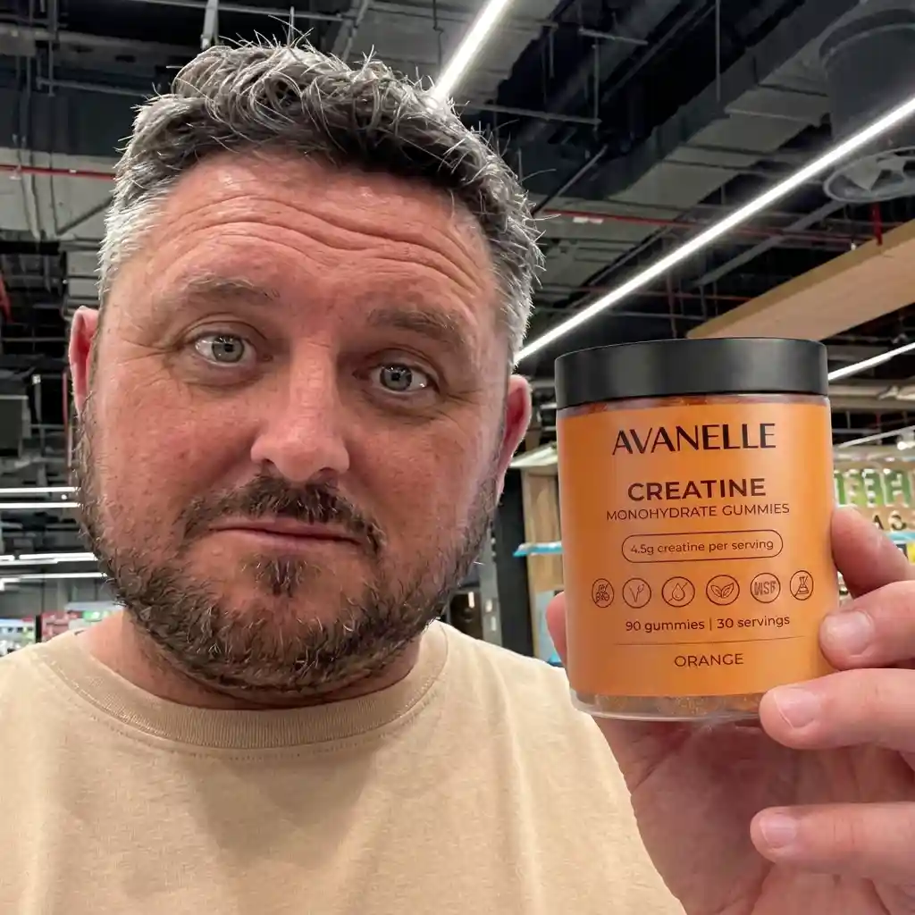 A man with salt-and-pepper hair holds up a container of Avanelle Creatine Monohydrate Gummies in a store.