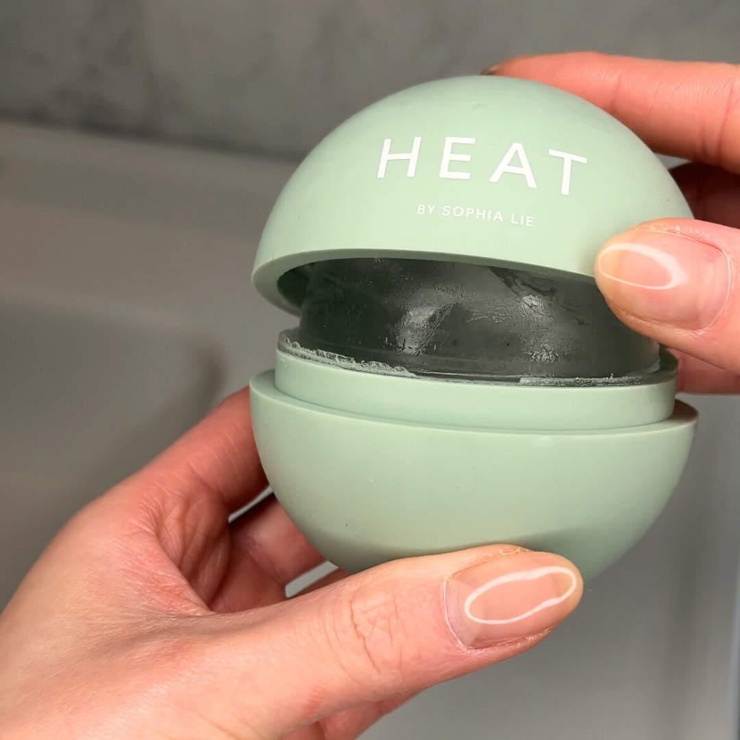 Hands holding a green spherical container labeled 'HEAT by Sophia Lie.'