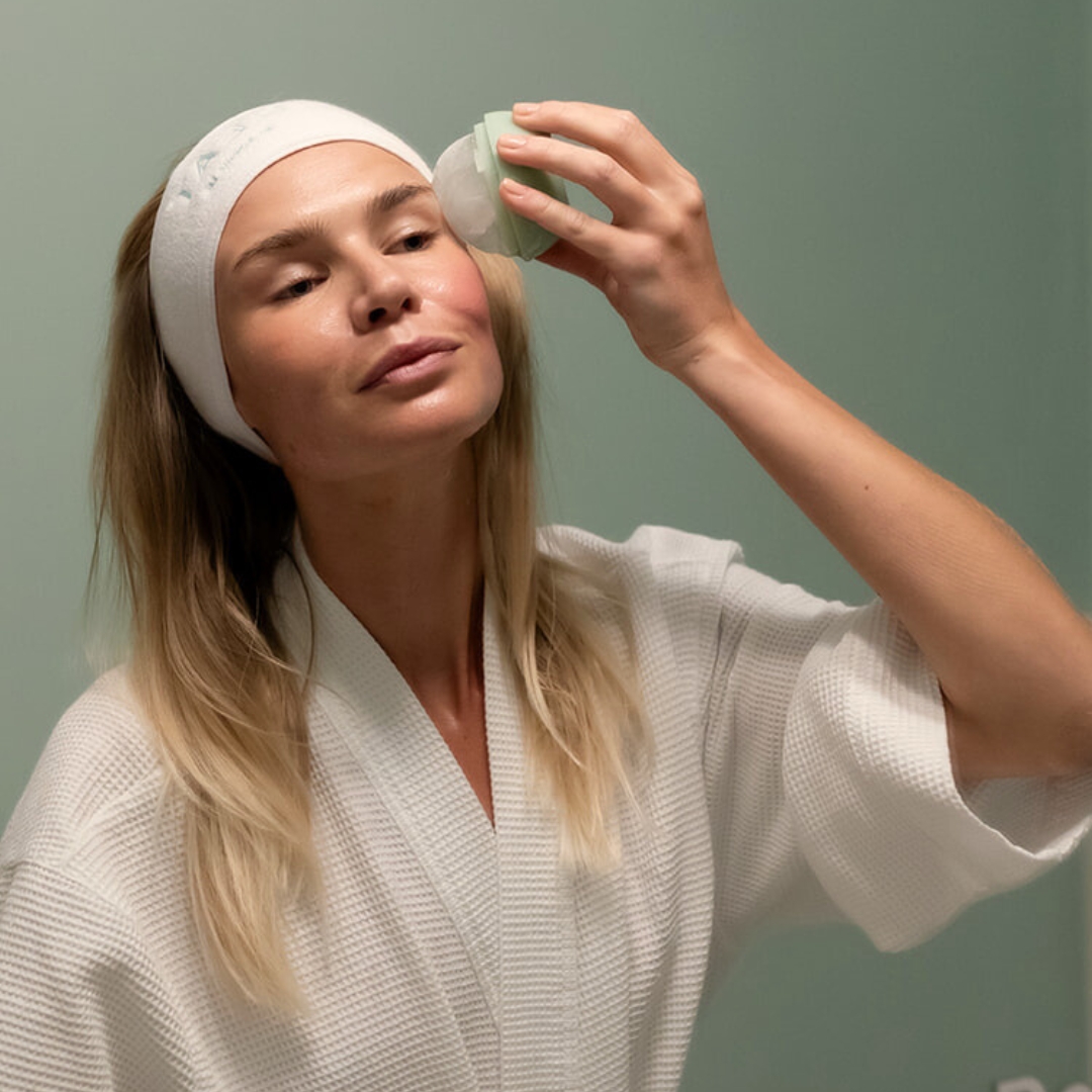 Person in a robe using a facial roller on their face.