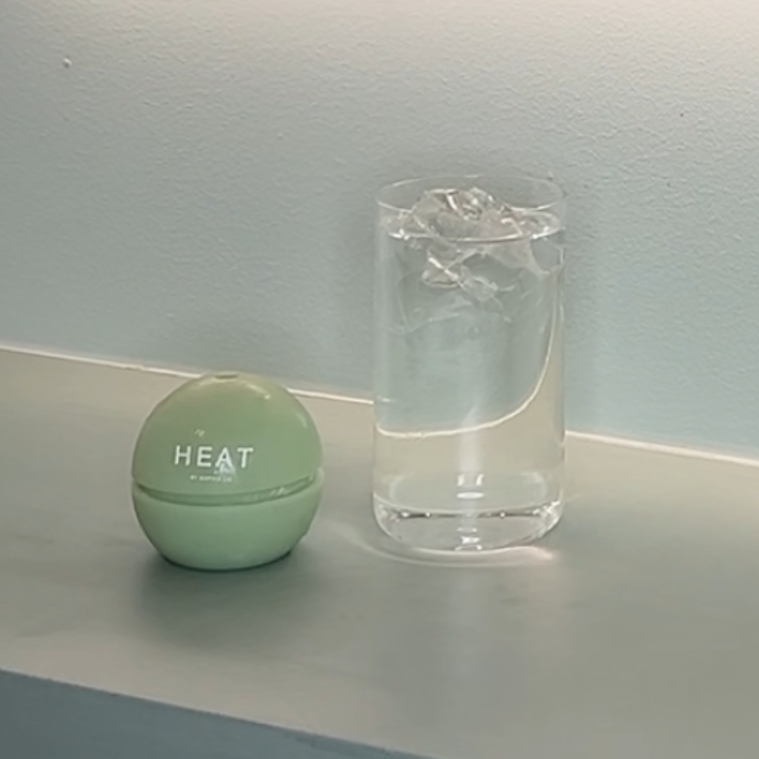 A green spherical container and a glass of water with ice on a surface.