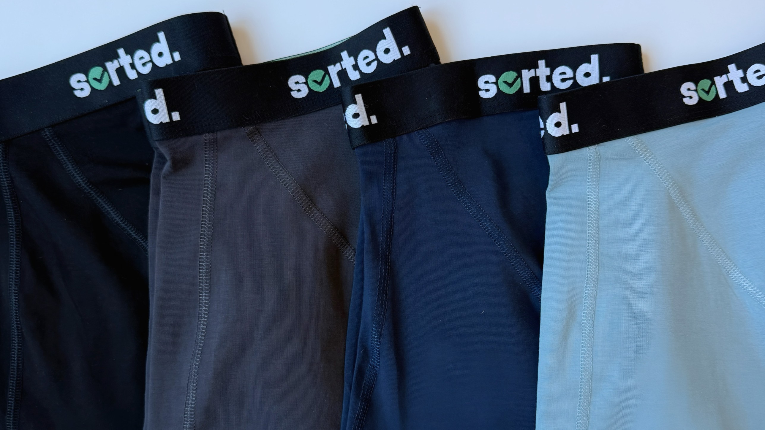 Four pairs of sorted brand boxer briefs in varying shades of black, grey, and blue.