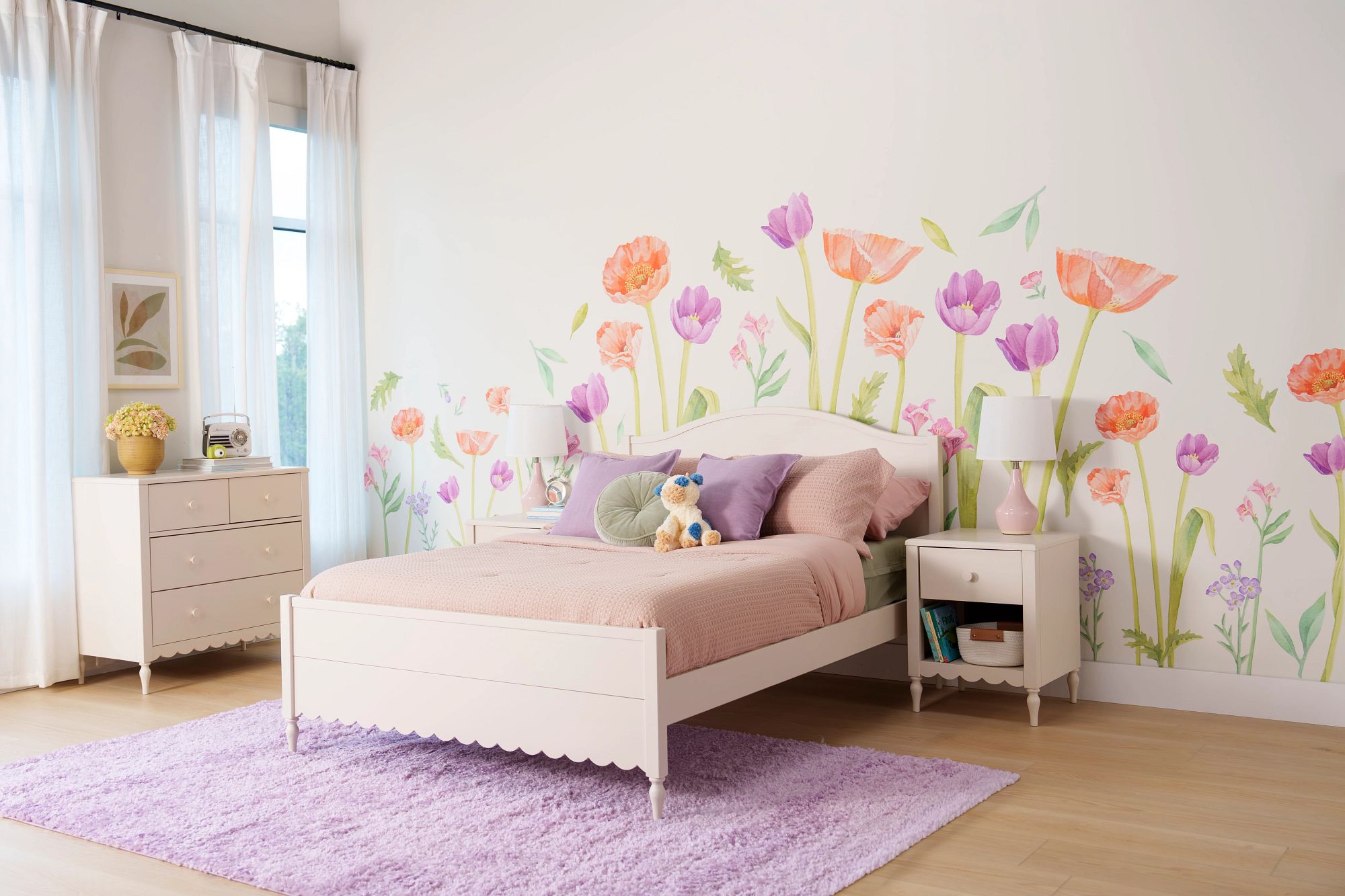 A white bedroom with orange and purple watercolor flower wall decals, with scalloped-trim bed, nightstand, and dresser.