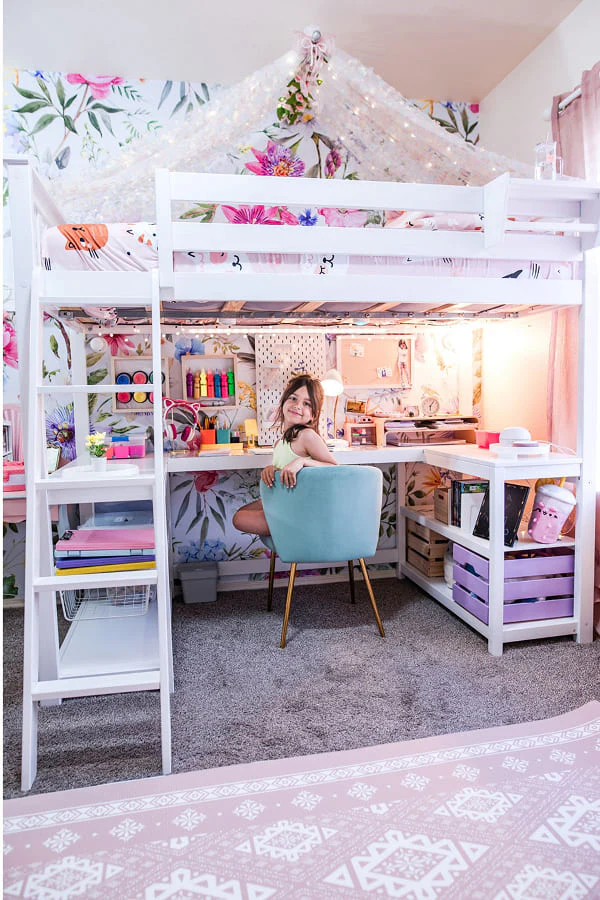 Child sitting at a desk under a loft bed with floral decor.