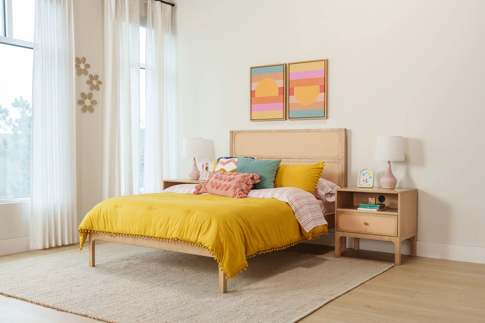 A bright bedroom with light wood rattan bed and matching nightstands. The bed has bright yellow bedding with teal and pink decor pillows, matching the colors in the room decor.