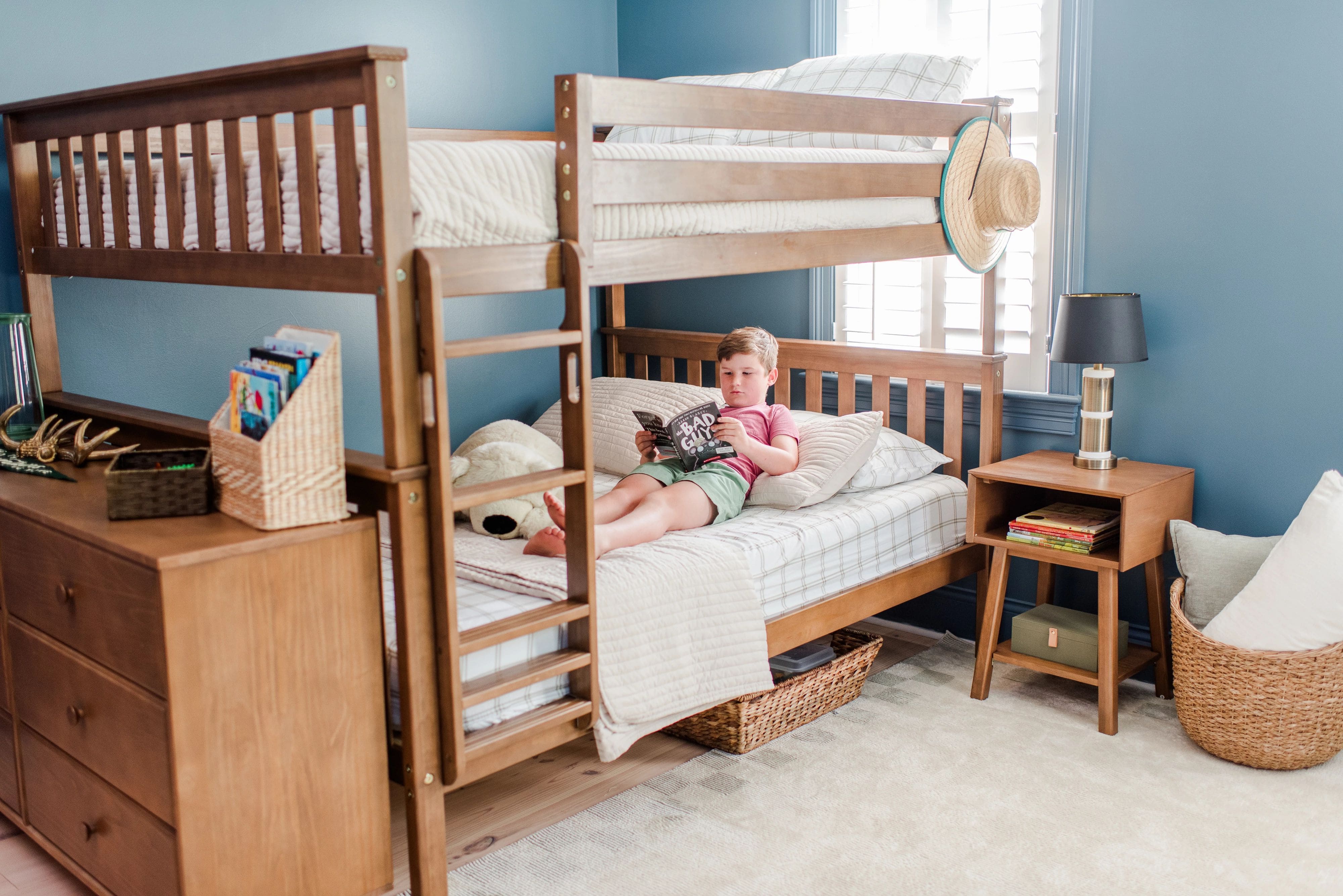 Child laying on bottom bunk of a queen bunk bed, reading a book in a blue room with beige decor.
