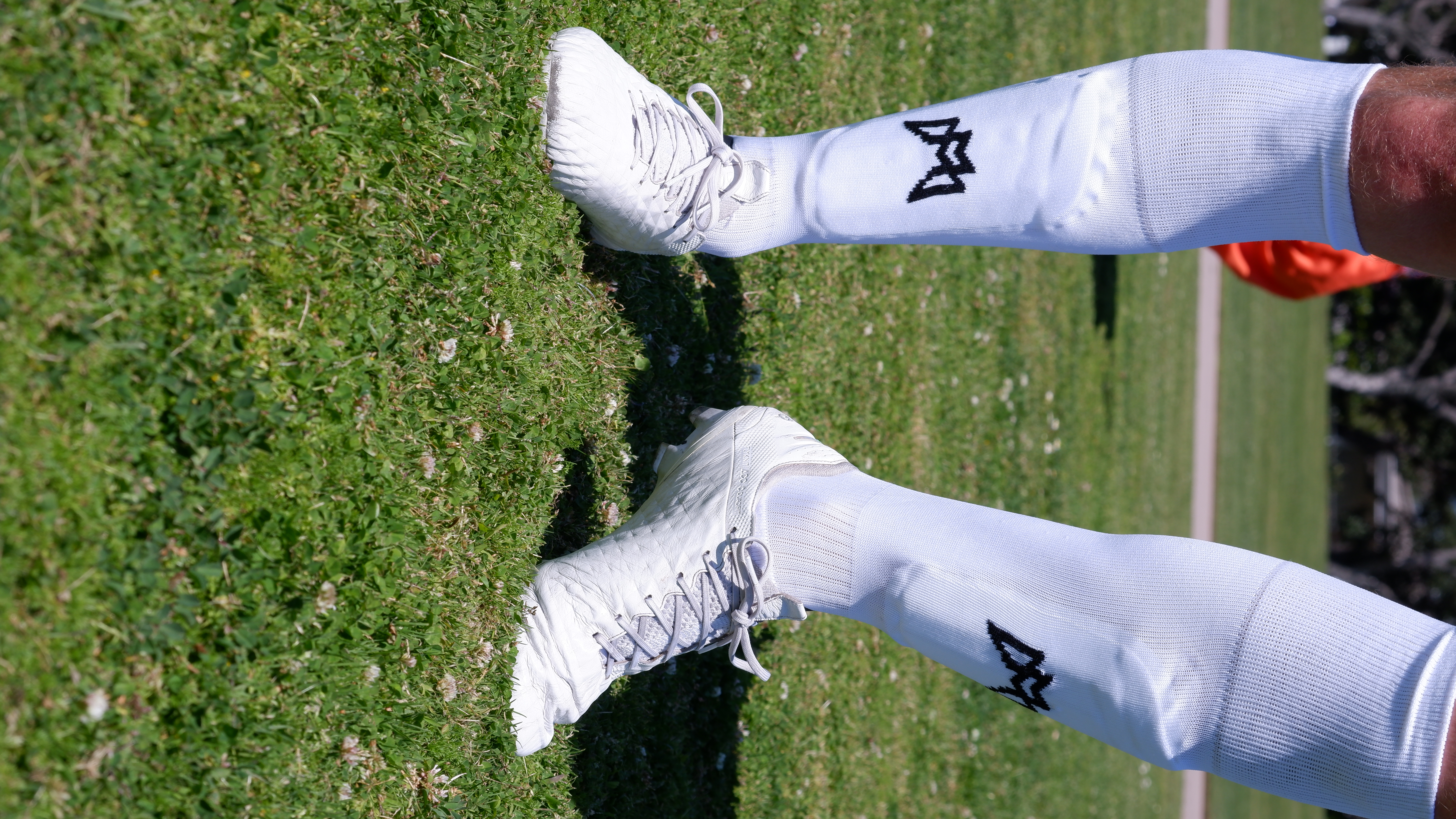 Soccer player wearing white cleats and socks on a grassy field.