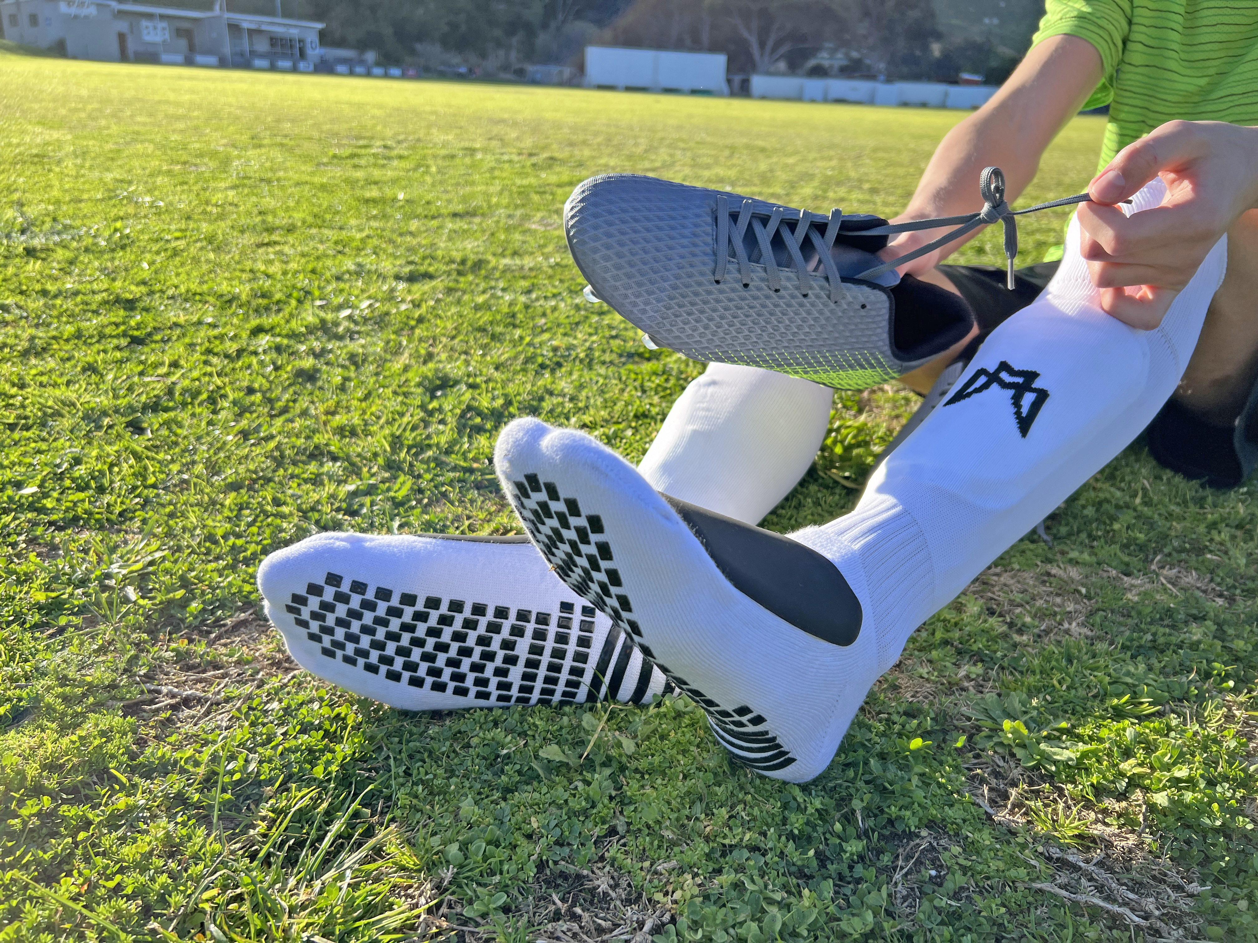 Person tying shoelaces on a soccer field, wearing grip socks.