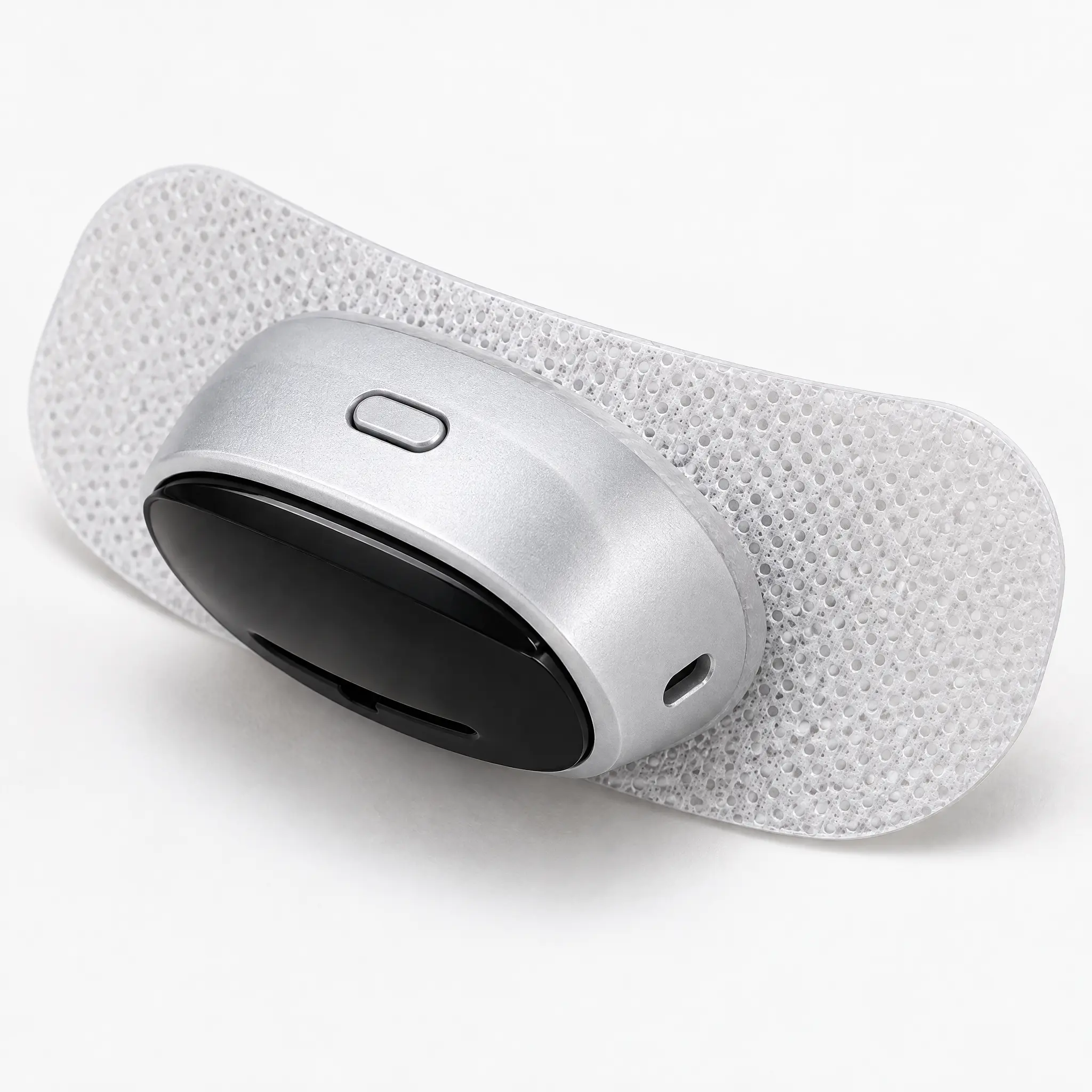 A small silver and black electronic device attached to a white porous adhesive patch on a white background.