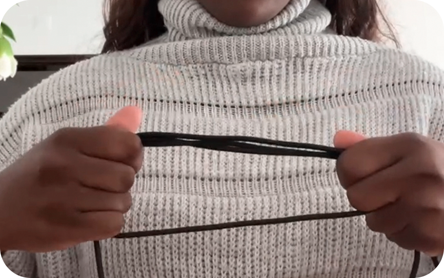 Person in a gray sweater holding a black string with both hands.