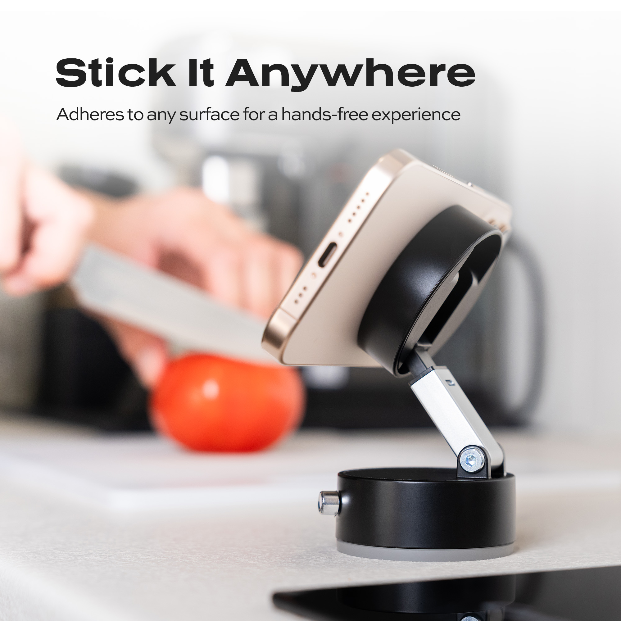 Phone on a black stand in a kitchen with a tomato and knife in the background.