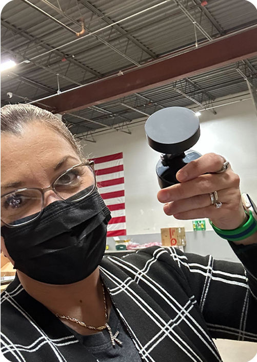 Person wearing a mask holding a black object in a warehouse with an American flag.