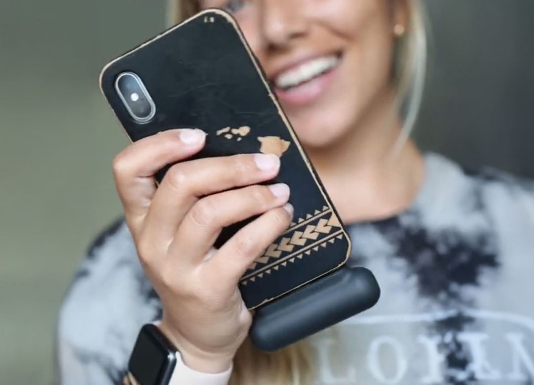 Person holding a phone with a patterned case, smiling in the background.