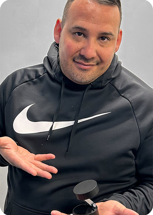 Person in a black hoodie holding a small black object, smiling.