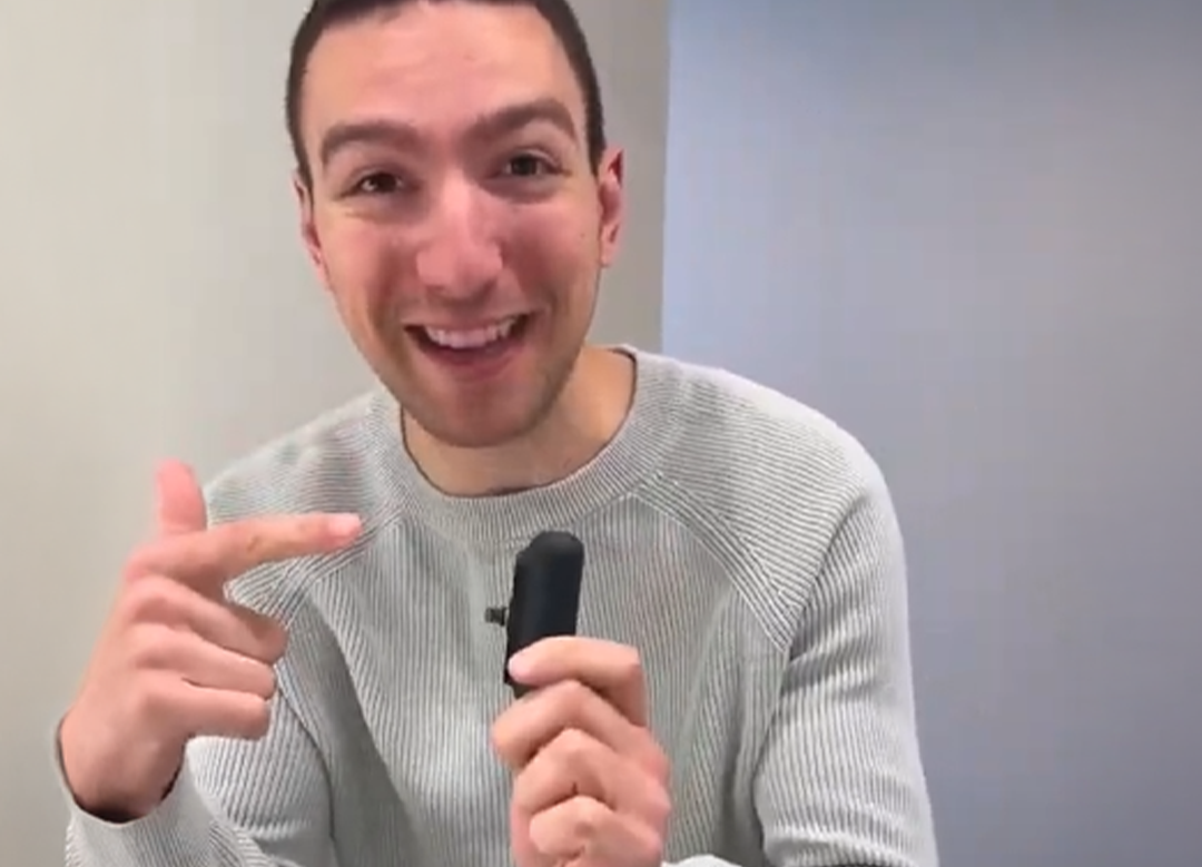 Person smiling and holding a small black object, pointing at it.