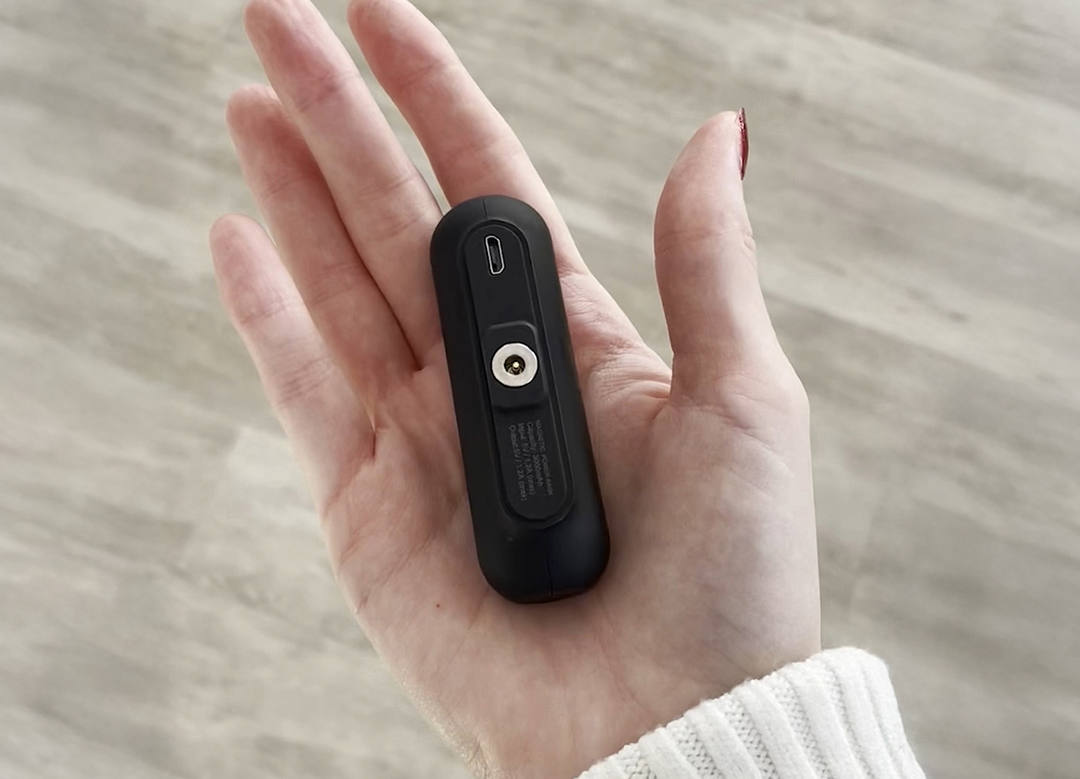 A hand holding a small black electronic device with a connector.