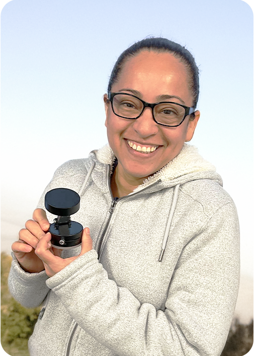 Person smiling, holding a small black object outdoors.