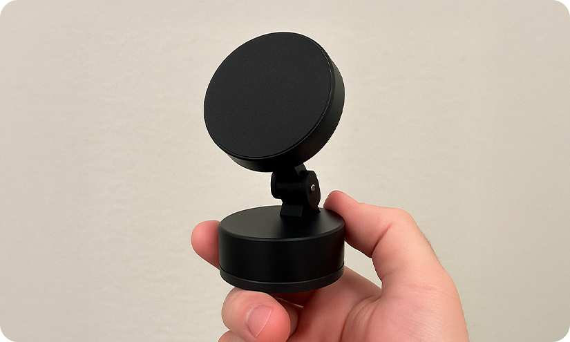 Hand holding a small black circular device with a stand.