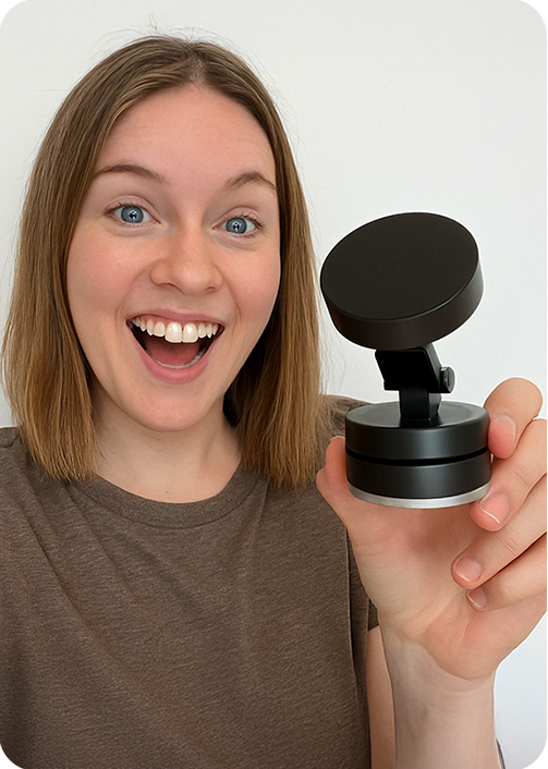 Person smiling and holding a small black device with a round top.
