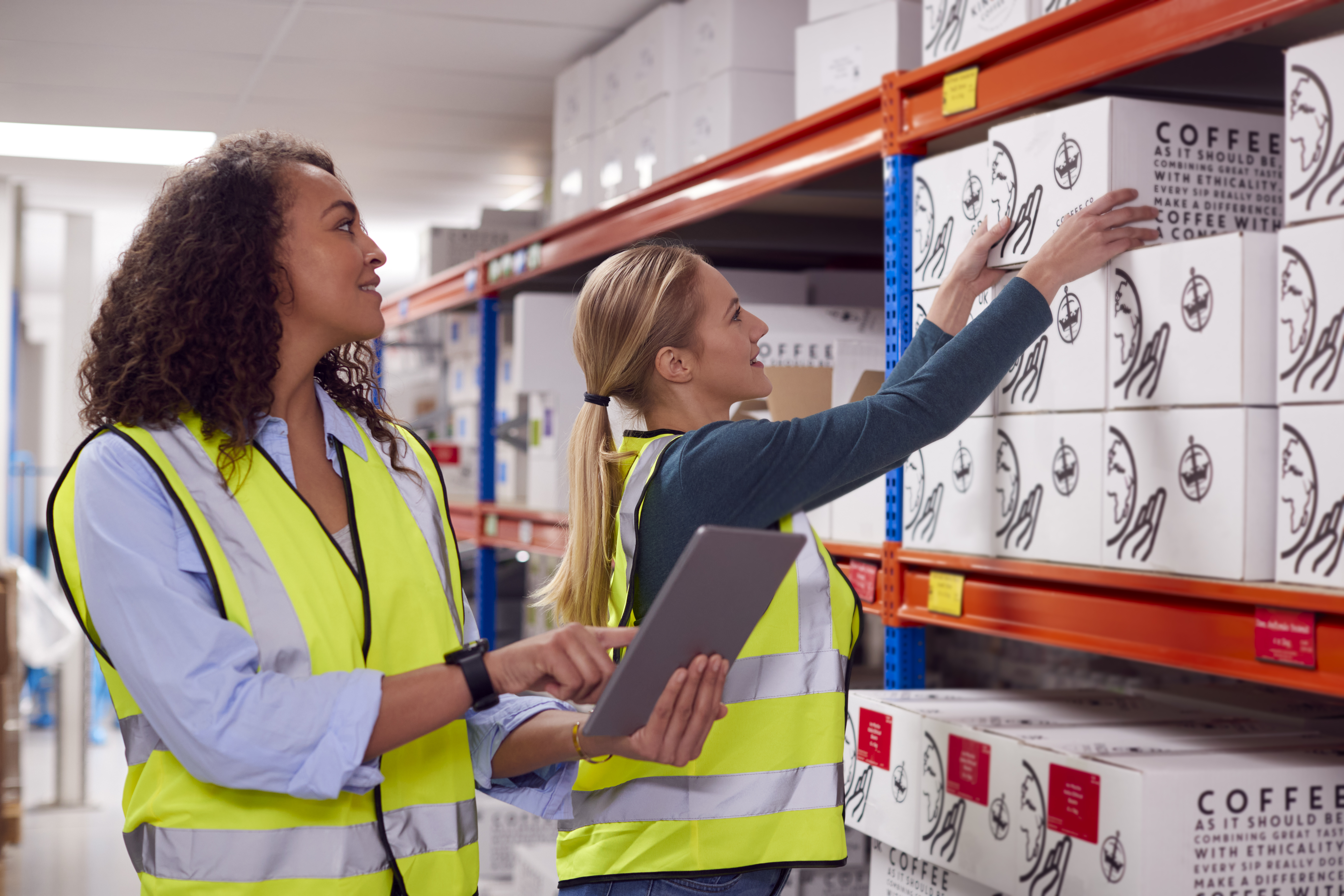 Two workers in safety vests organizing boxes on shelves.