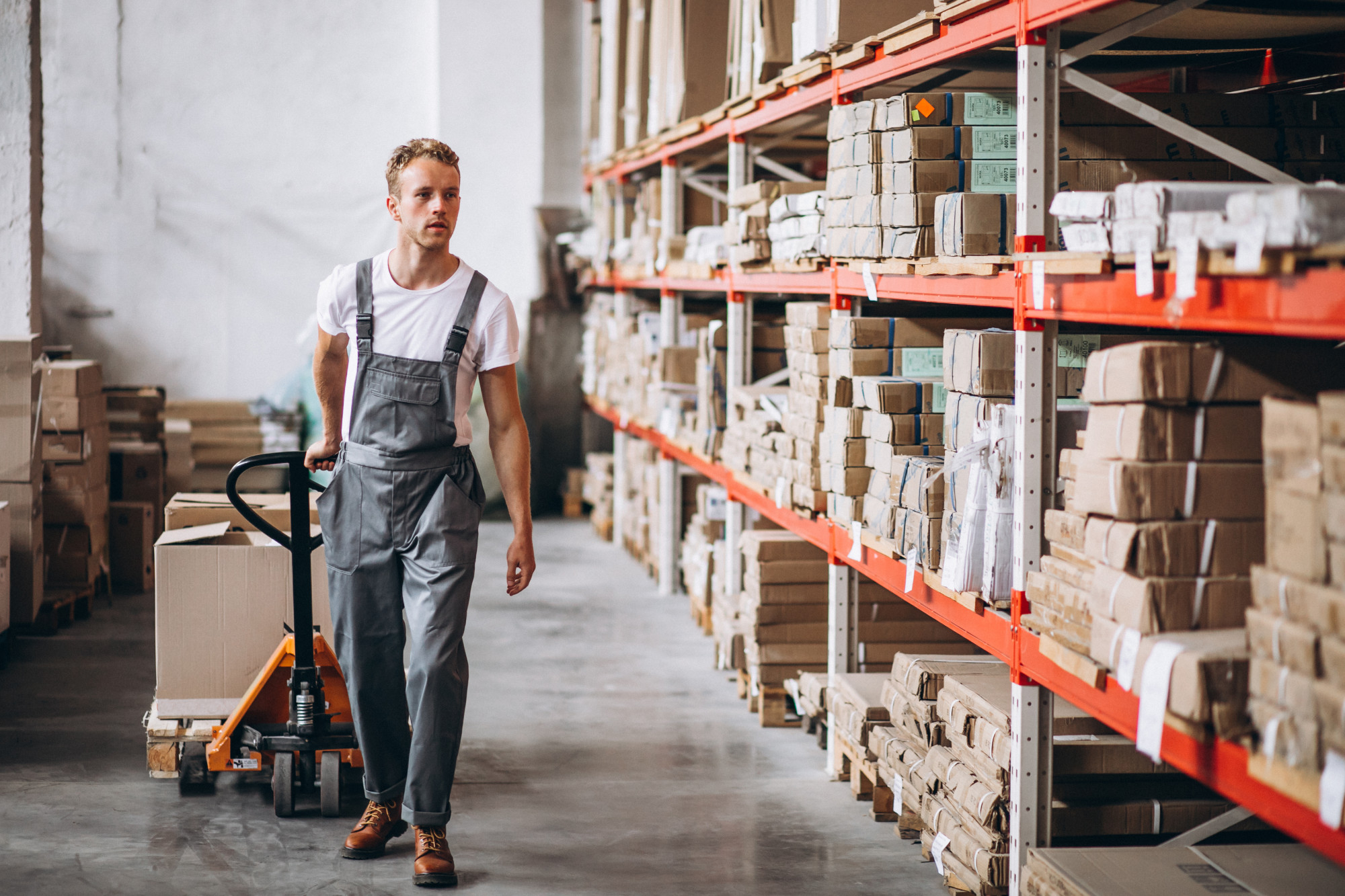 Man in work attire moving boxes on a pallet jack in a warehouse.