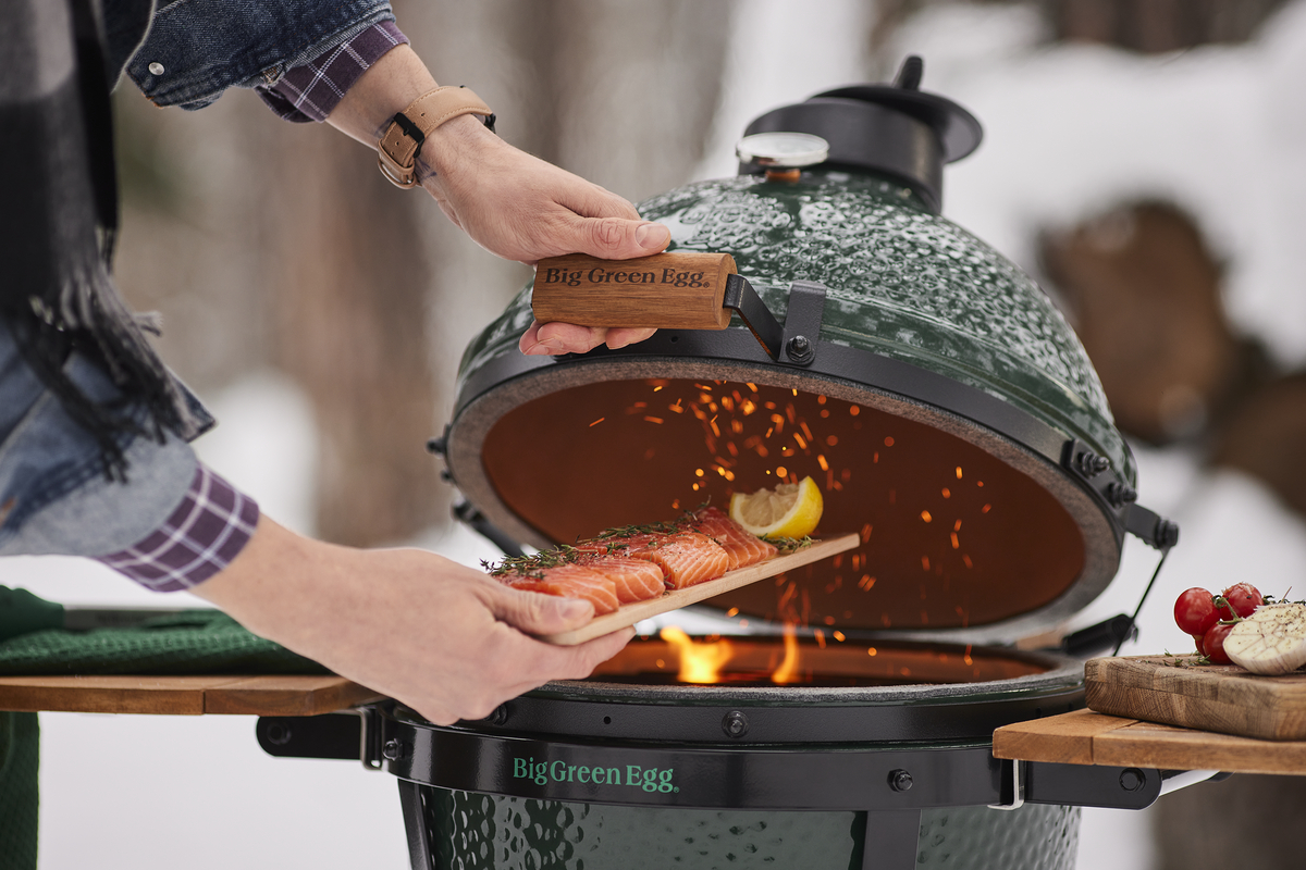 Person grilling salmon on a Big Green Egg barbecue in snowy outdoors.