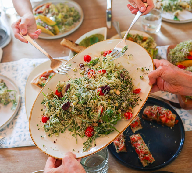 A plate of pasta topped with fresh sprouts held above a set table