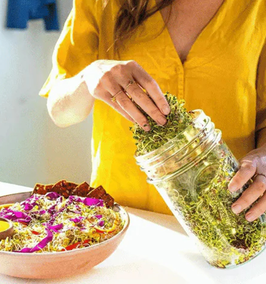 Hands tipping a jar of fresh sprouts onto a bowl of salad