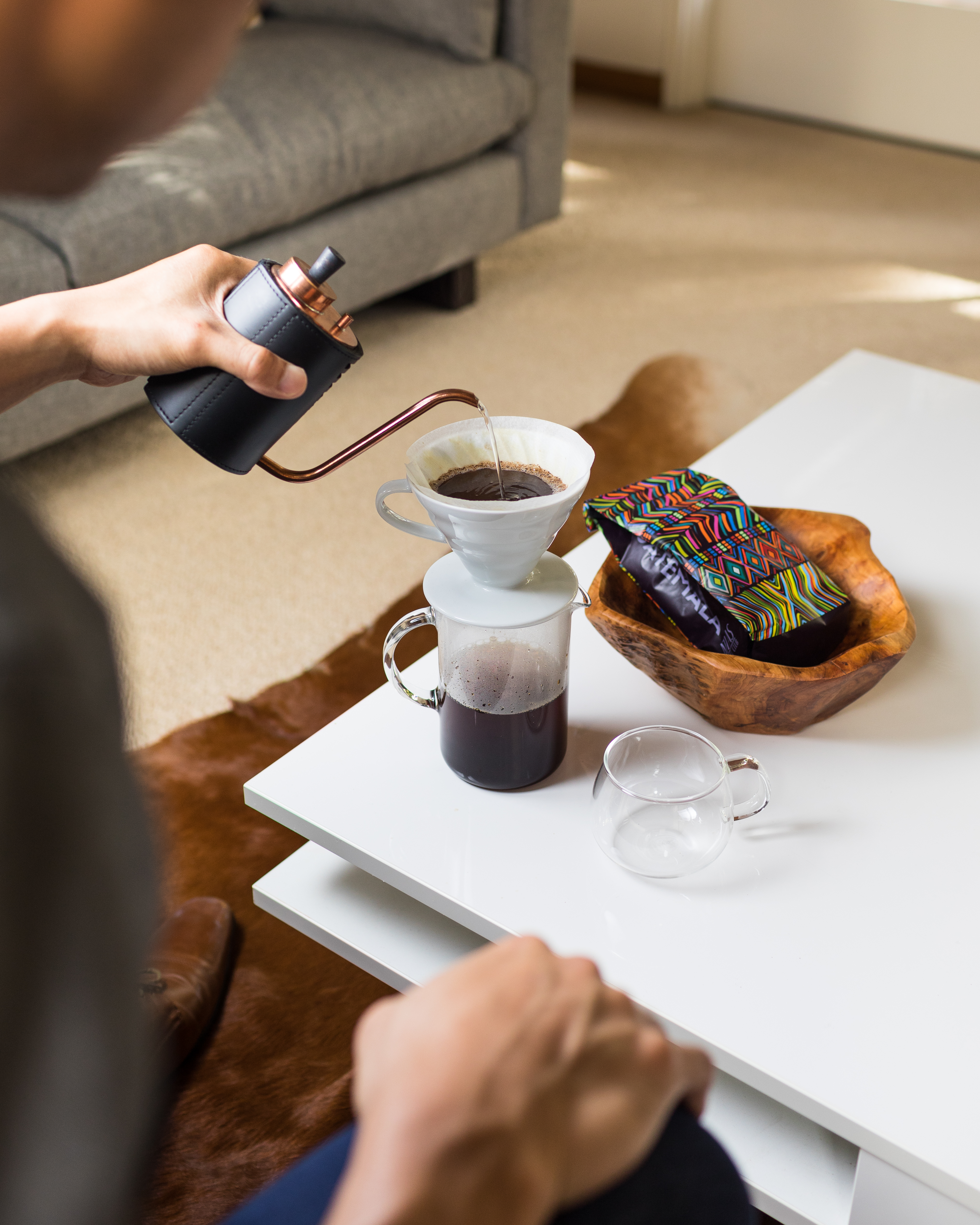 Person pouring coffee with a gooseneck kettle into a pour-over on a table.