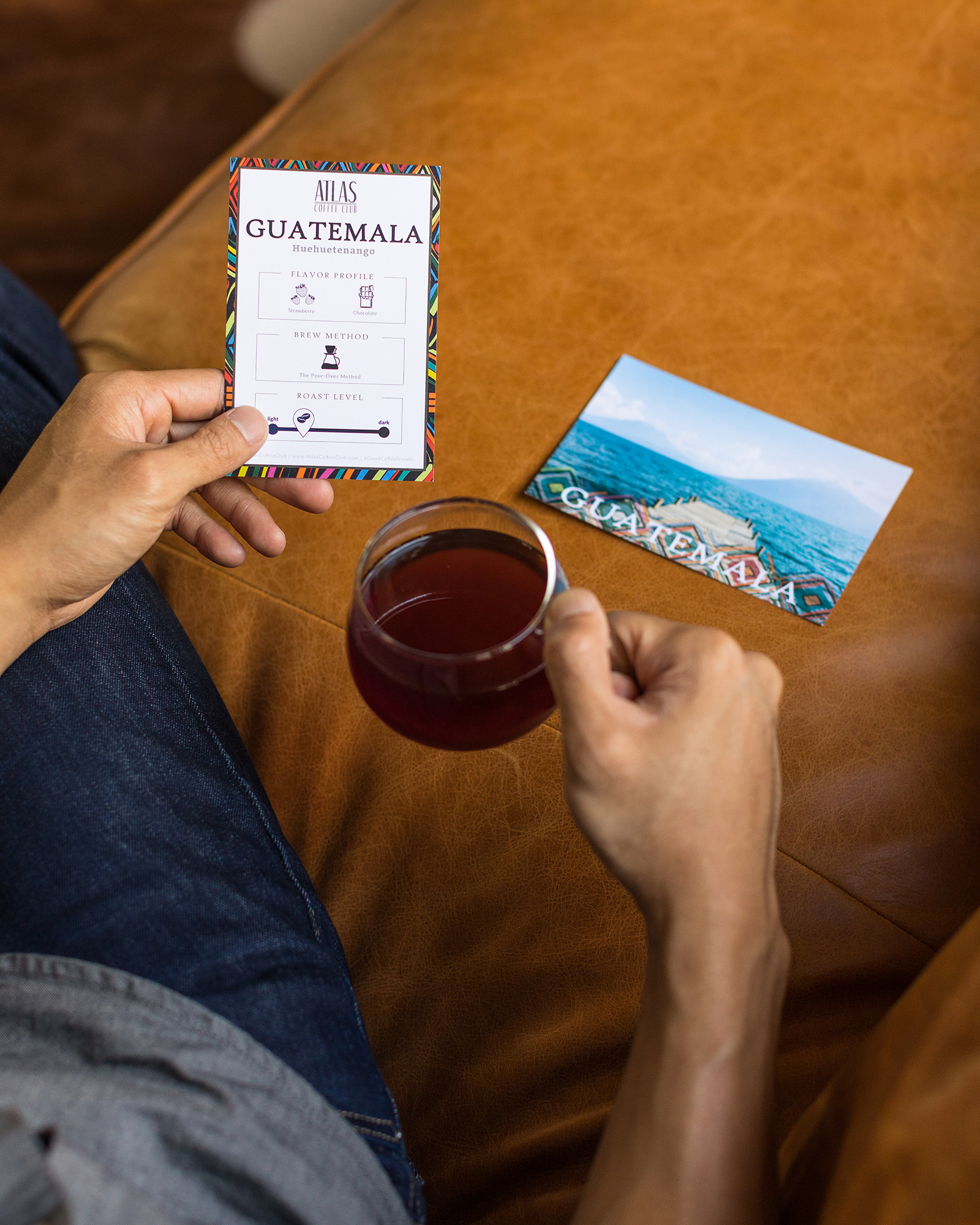 Person holding coffee card and cup, postcard nearby.
