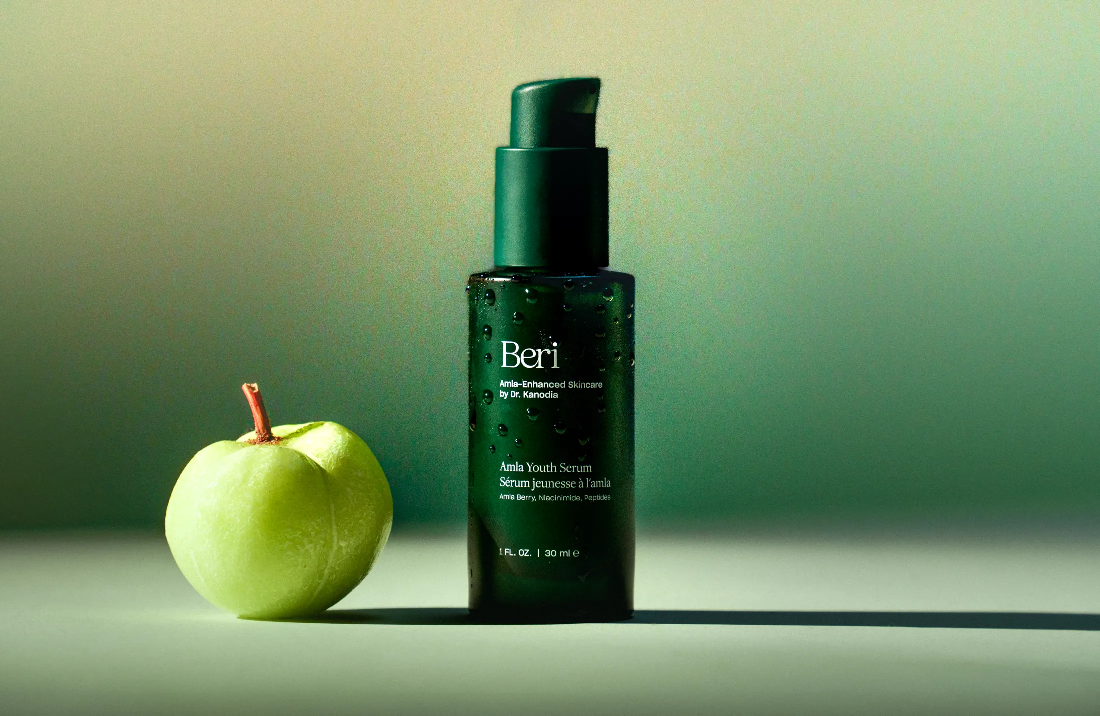 Green apple next to a dark green skincare serum bottle.