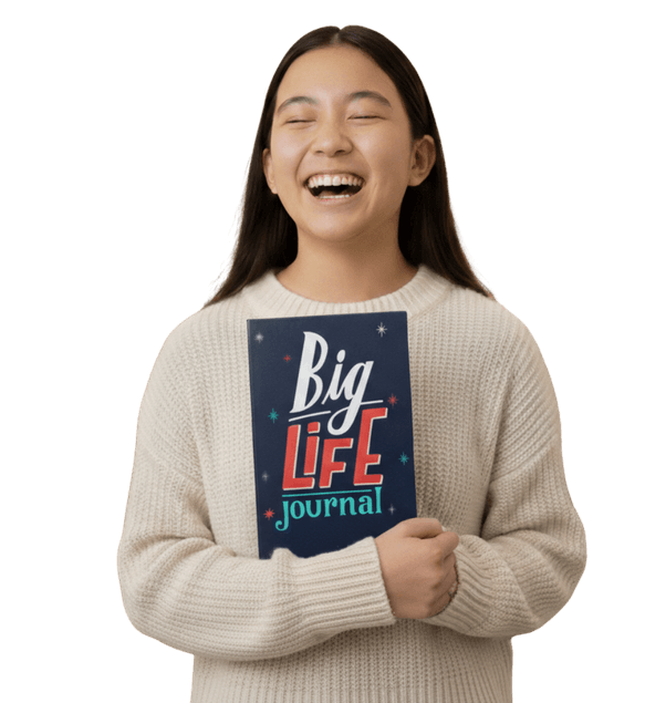 A young woman in a cream sweater laughs while holding a book titled 'Big Life Journal'.