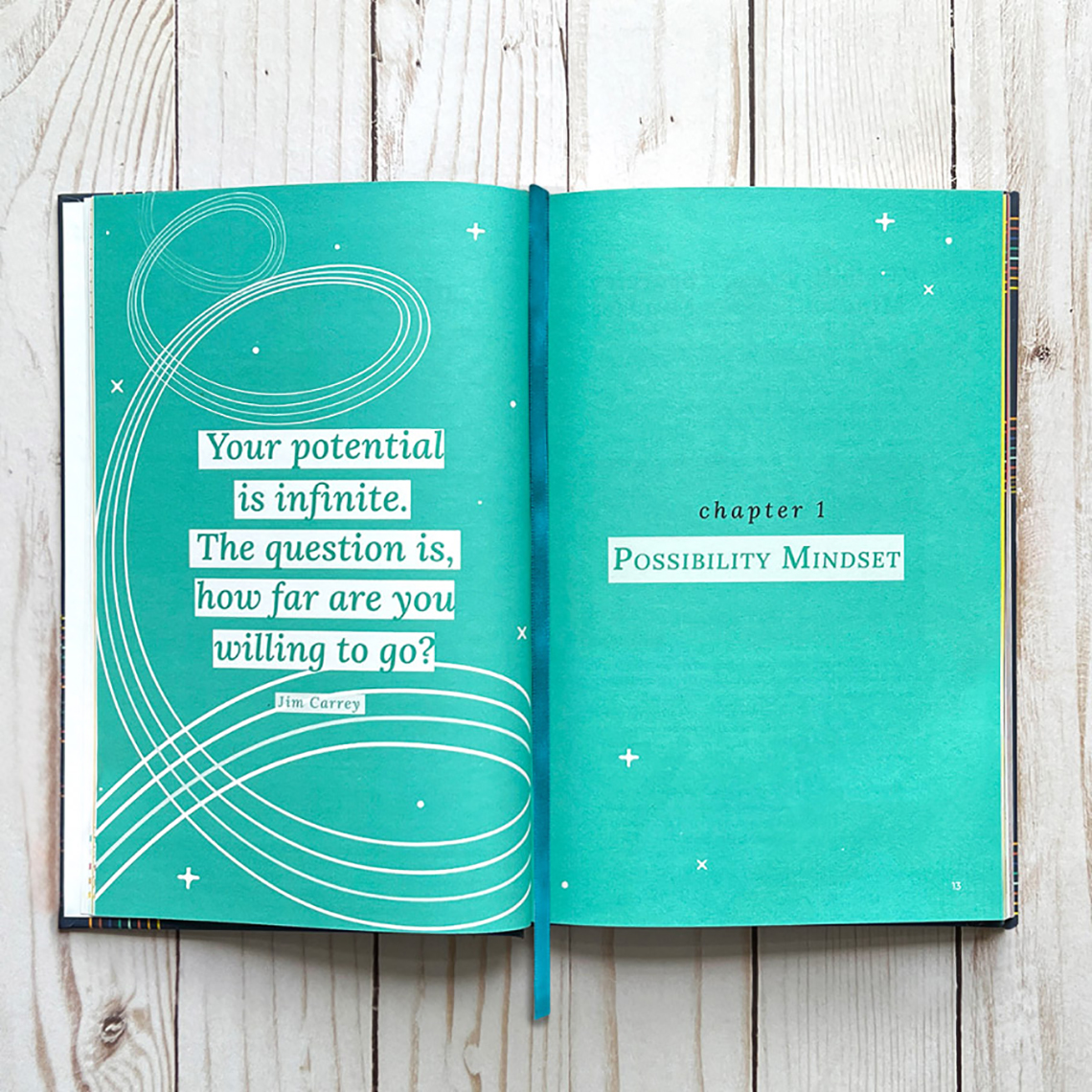 An open book on a wooden surface with a Jim Carrey quote on a teal page.