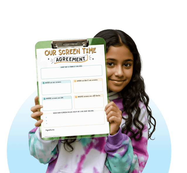 A young girl in a tie-dye hoodie smiles while holding up a blank 'Our Screen Time Agreement' worksheet.