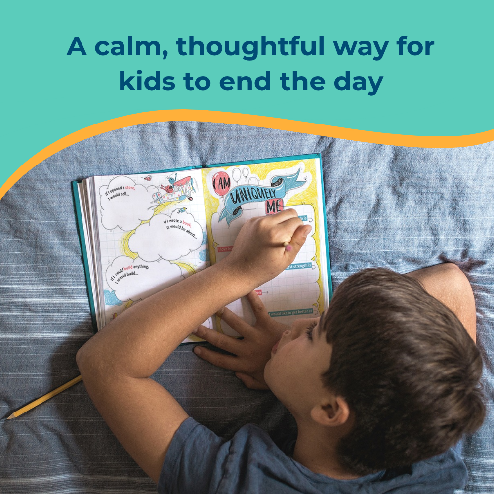An overhead view of a young boy lying on his bed, writing in a colorful journal with a pencil.
